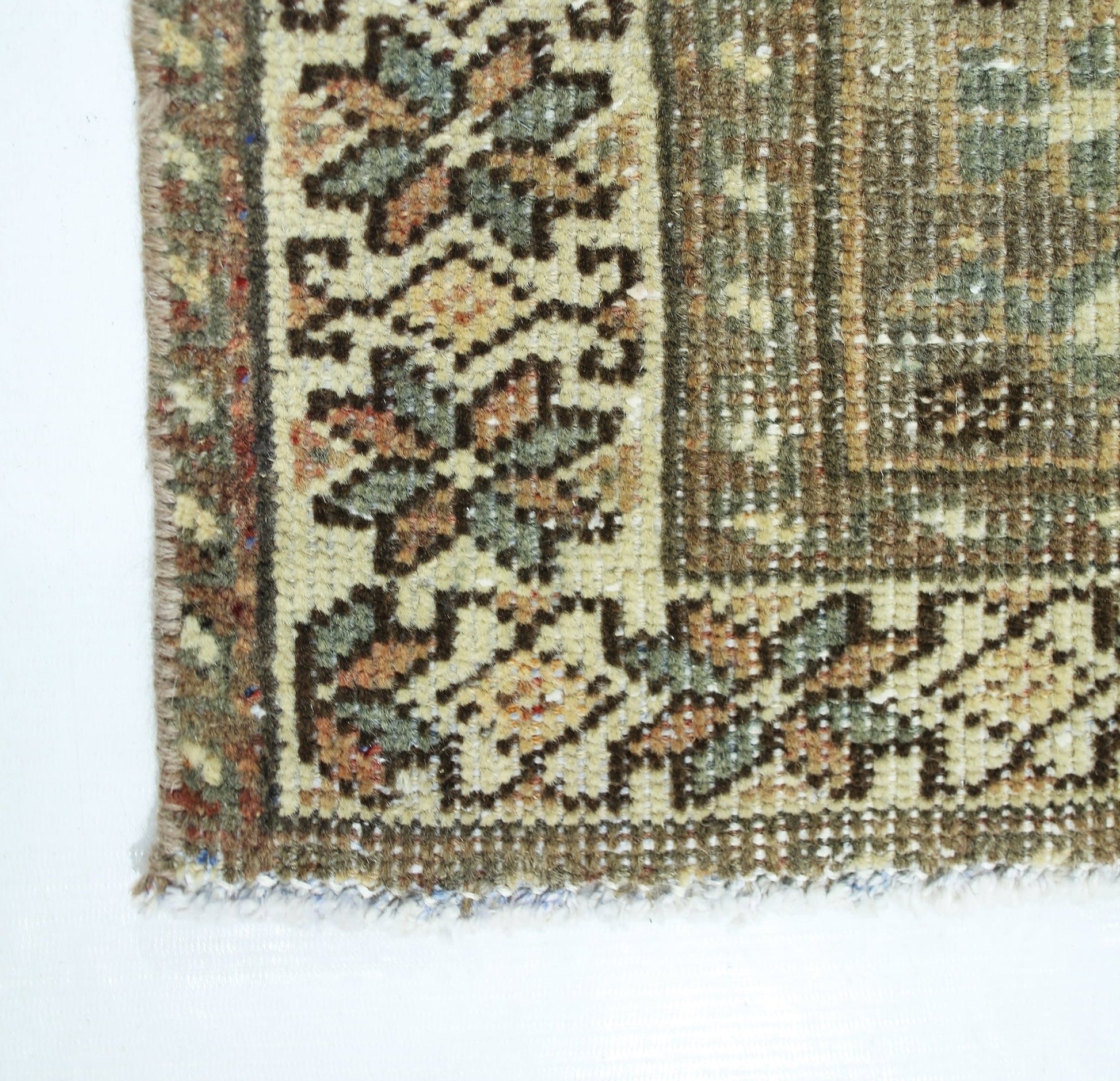 A corner detail of a vintage Persian Qashqai rug featuring intricate floral patterns in muted tones.