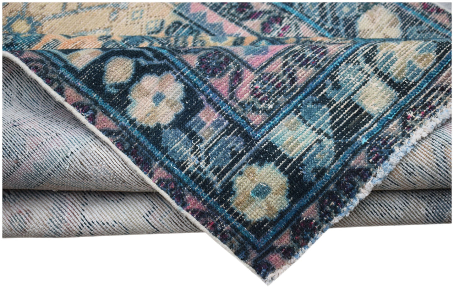 A folded vintage Persian rug featuring a blue and pink floral pattern with a worn texture.