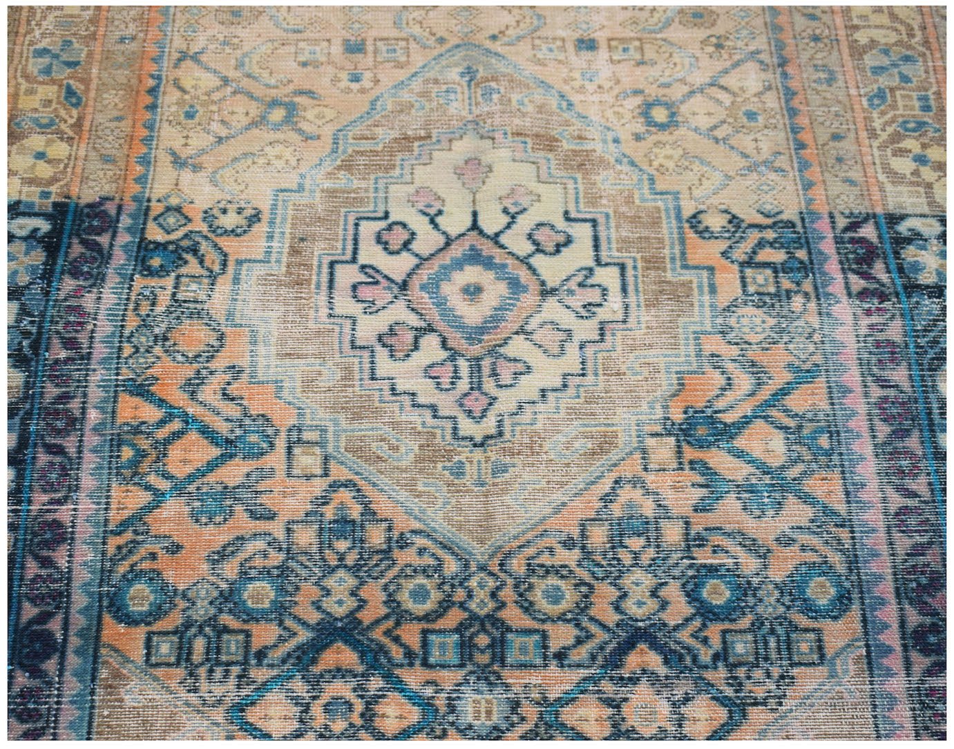 A vintage handwoven Persian rug featuring a central geometric medallion in blue, orange, and tan.