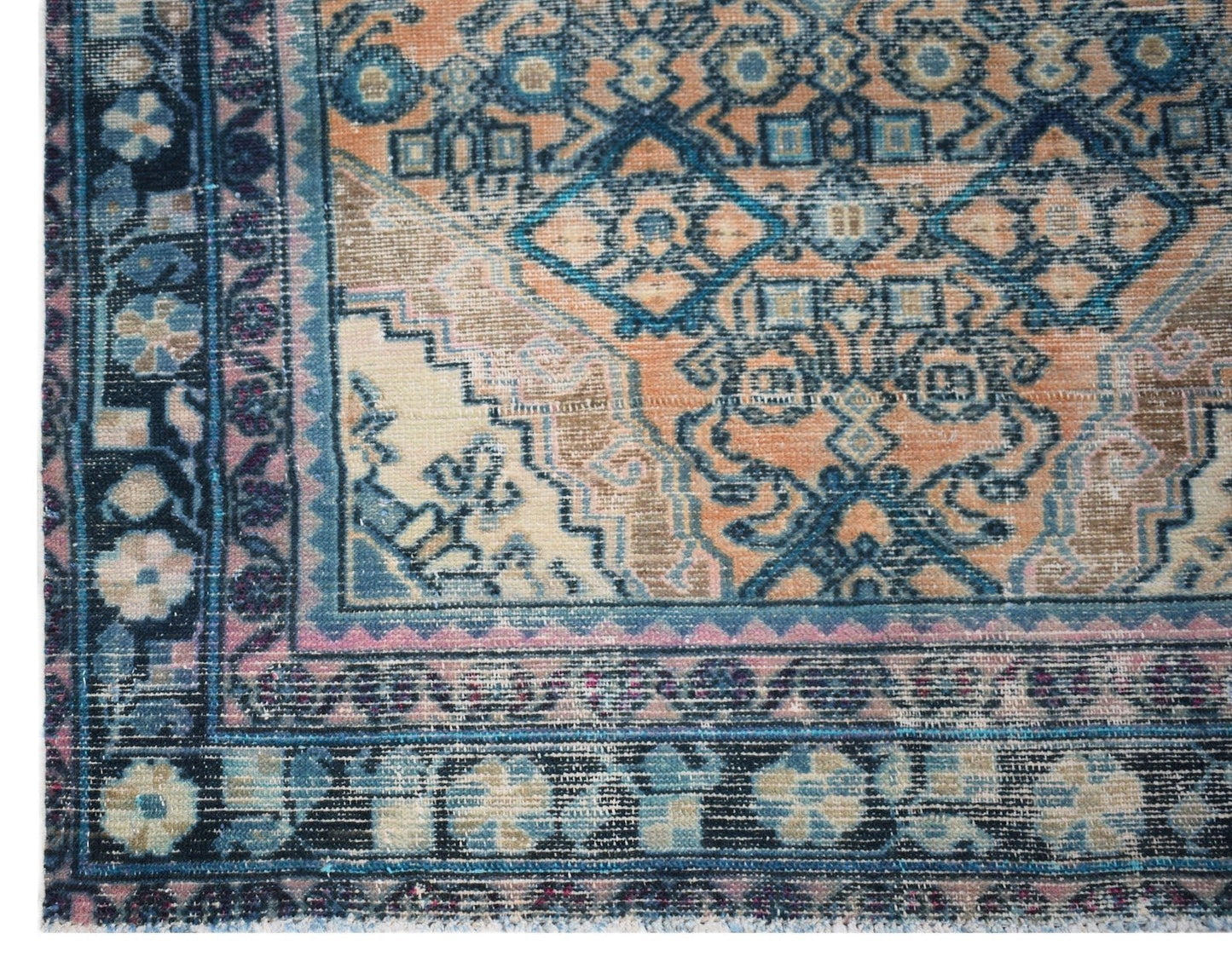 A vintage handwoven Persian rug featuring a distressed geometric pattern in blue, orange, and pink.