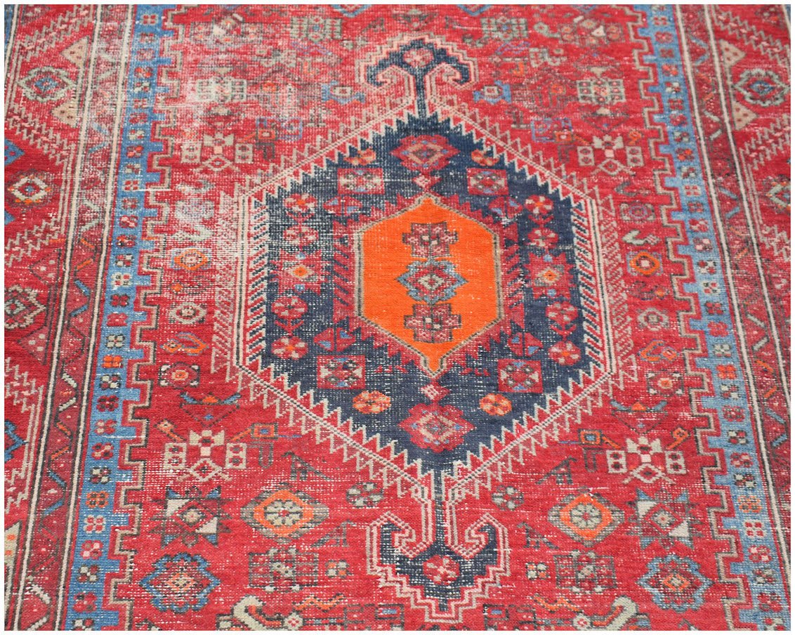 A vintage handwoven Persian rug featuring a central orange medallion on a dark blue and red field.