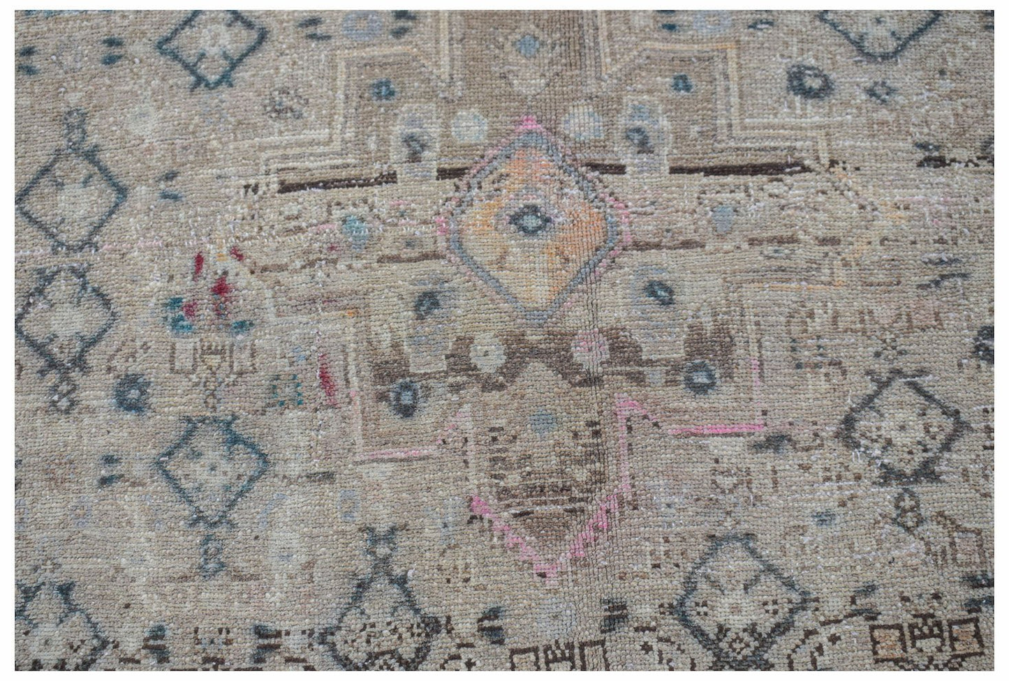 A vintage handwoven Persian rug featuring a faded geometric pattern in neutral and muted tones.