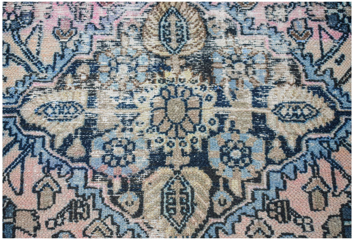 A vintage handwoven Persian rug featuring a faded floral medallion pattern in blue, pink, and tan.