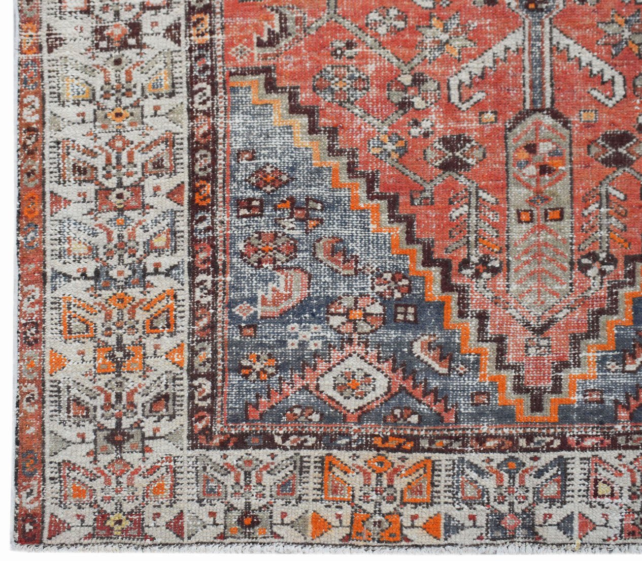 A handwoven vintage Persian rug featuring a geometric pattern in shades of red, blue, and cream.