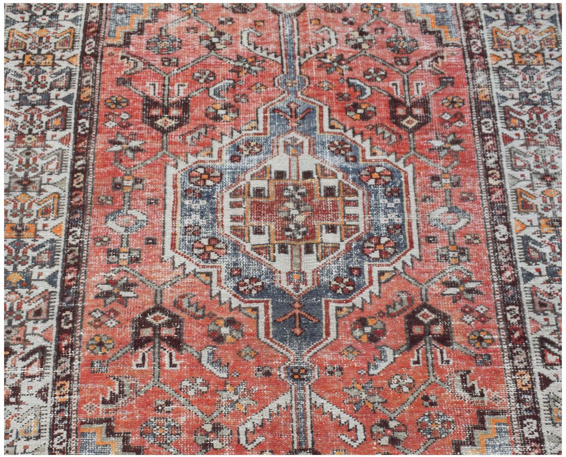 A vintage handwoven Persian rug featuring a central geometric medallion in red, blue, and cream.