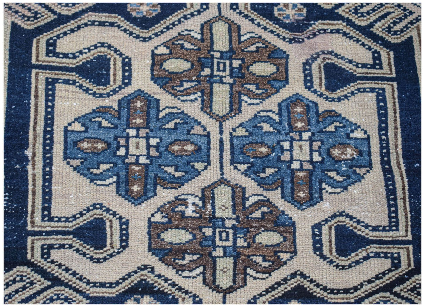 A vintage handwoven Persian rug featuring a geometric floral pattern in blue, brown, and cream.