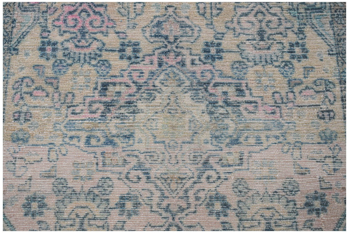 Vintage Persian rug with a distressed pattern in blue and pink on a cream background.