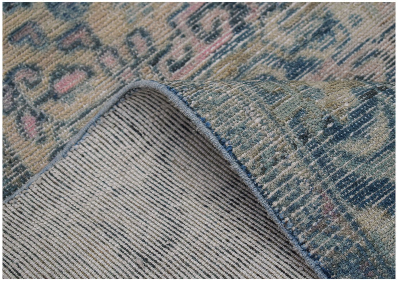 A handwoven vintage Turkish rug featuring a faded blue and cream floral pattern on wool.