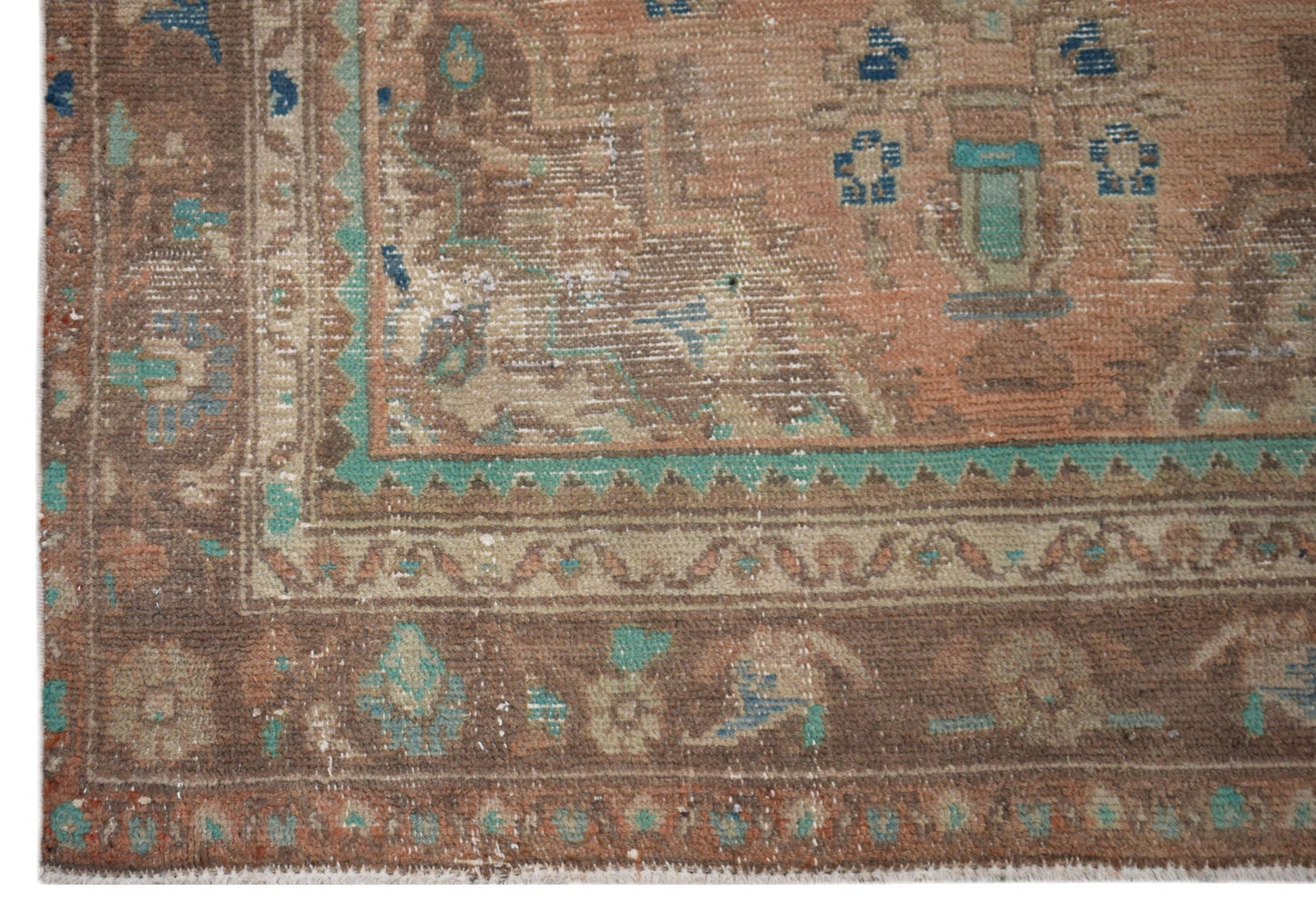 A vintage Persian Sarouk rug featuring a worn, handwoven pattern in brown, orange, and teal tones.
