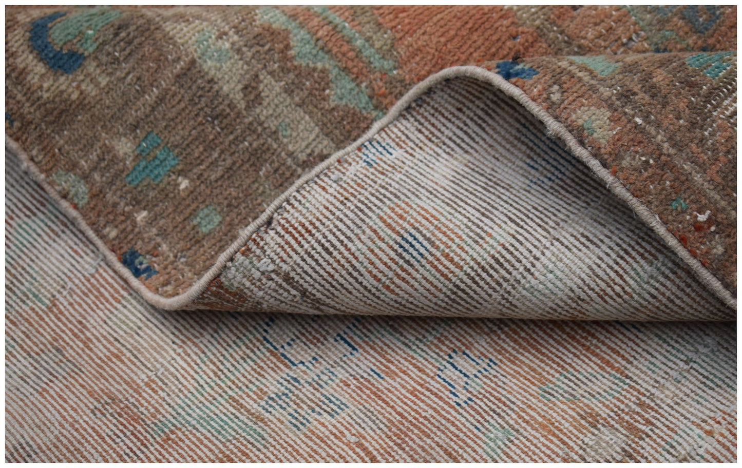 A close-up of a vintage Persian Sarouk rug showing its handwoven wool texture and worn underside.