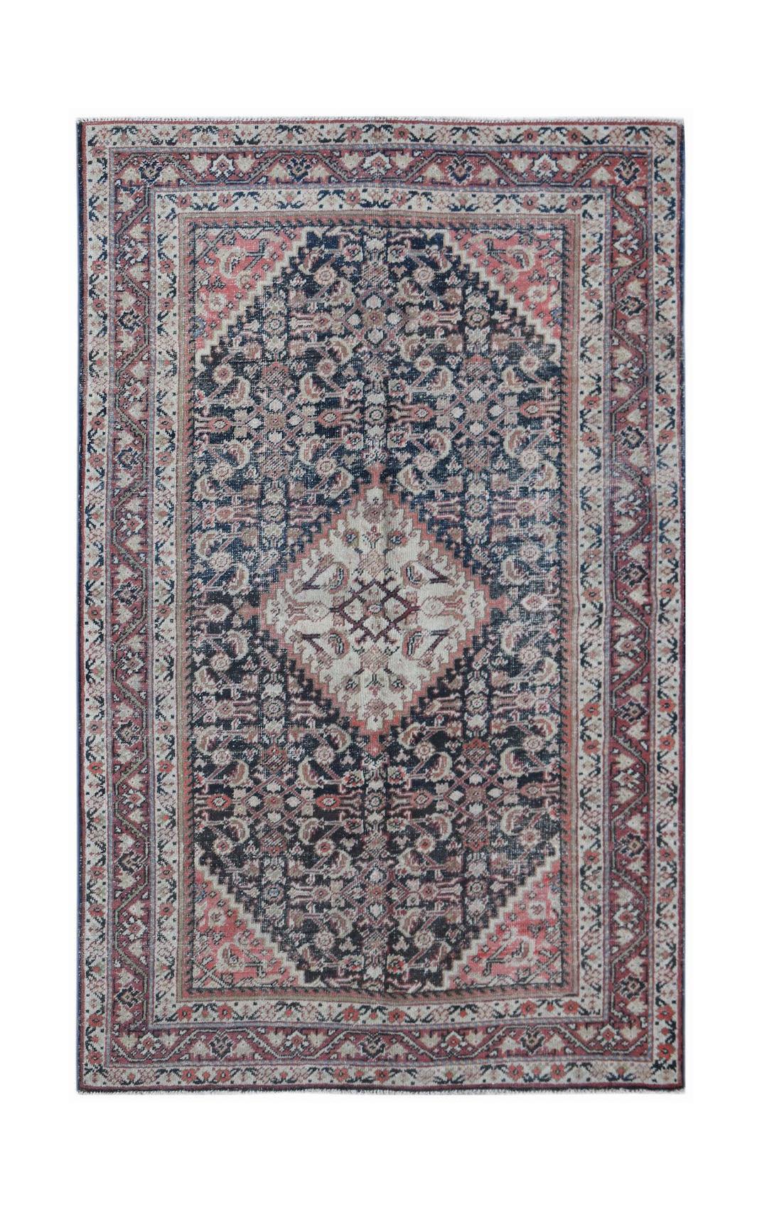 A rectangular vintage Persian rug featuring a central diamond medallion in navy, pink, and cream.