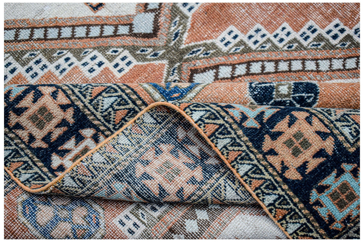 A handwoven vintage Persian rug featuring geometric patterns in shades of orange, blue, and cream.