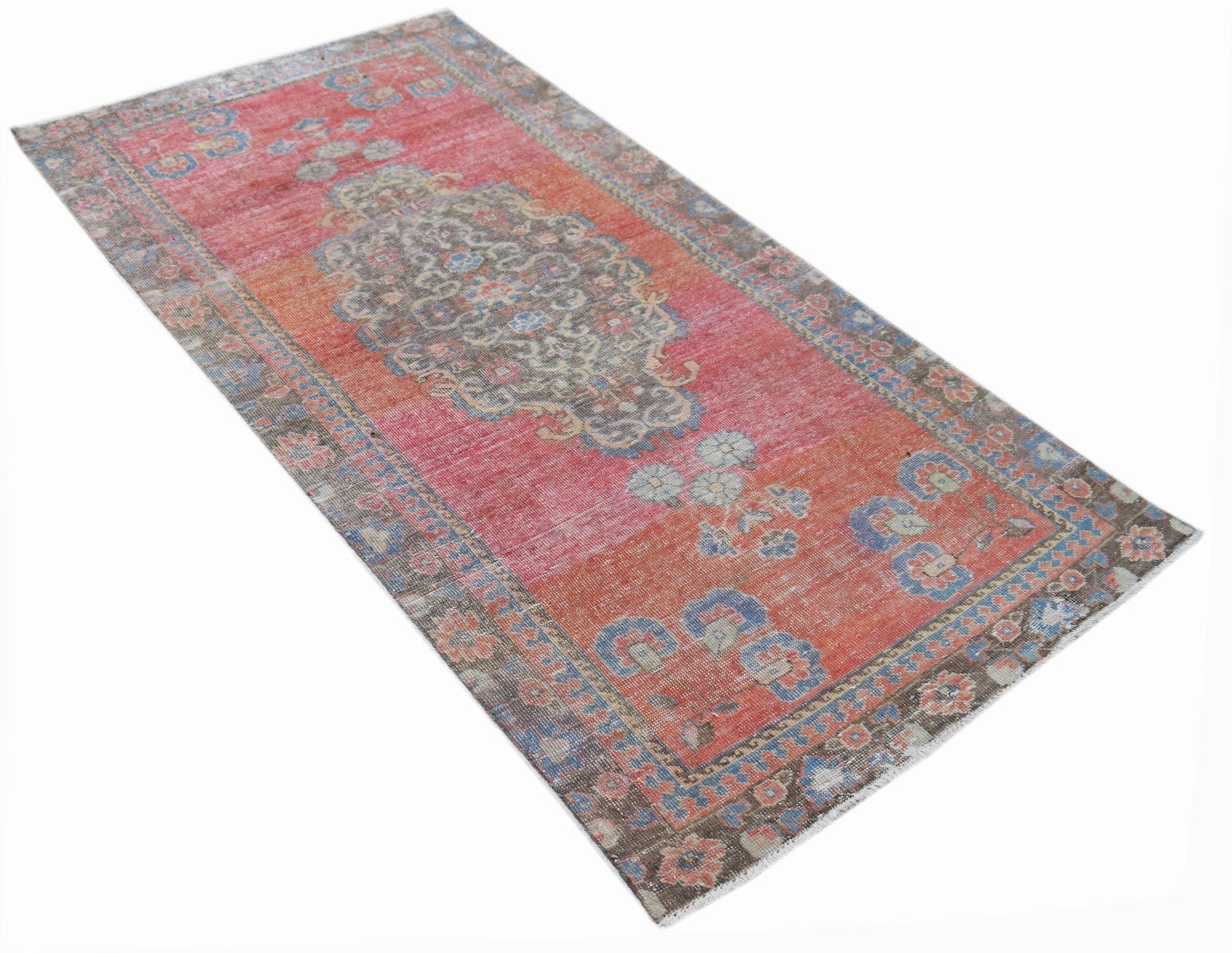 A vintage handwoven Persian rug featuring a faded red and orange floral pattern.