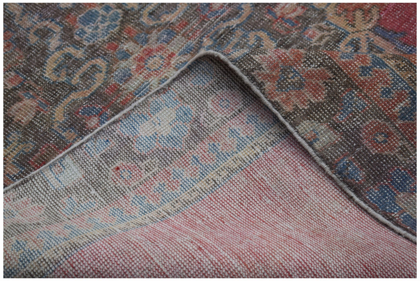A corner of a vintage handwoven Persian rug showing its worn wool pile and cotton foundation.