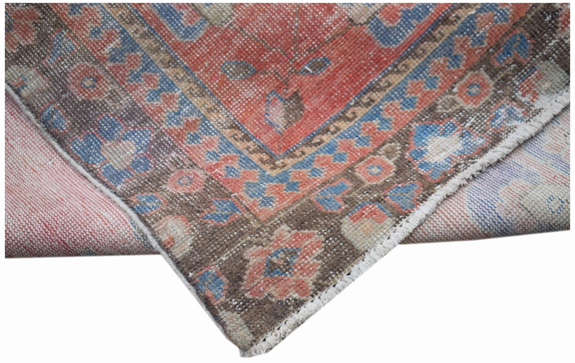 A vintage handwoven Persian rug featuring a floral pattern in faded red, blue, and brown tones.
