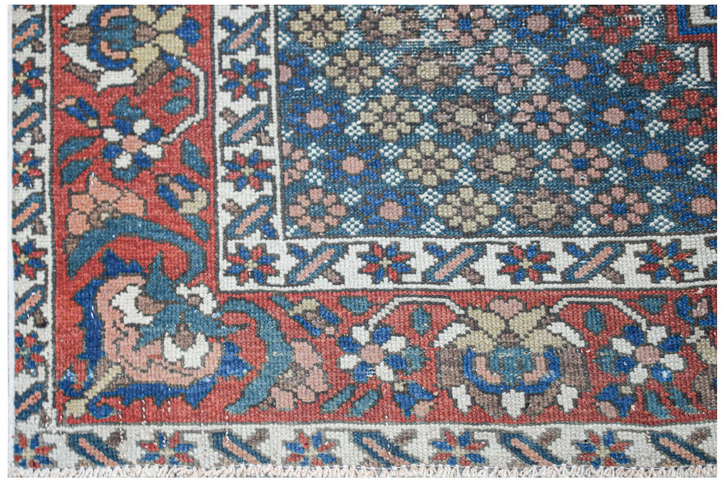 A vintage handwoven Persian rug featuring a blue floral field with a red patterned border.