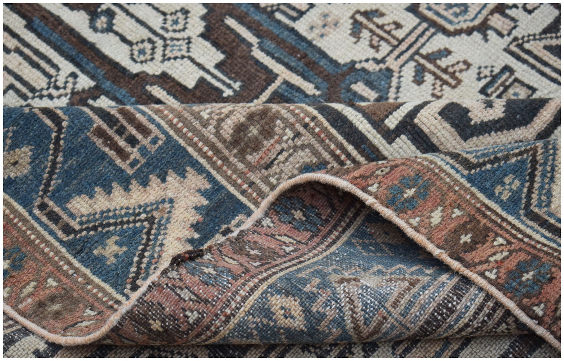 A handwoven vintage Persian rug featuring geometric patterns in shades of blue, brown, and cream.