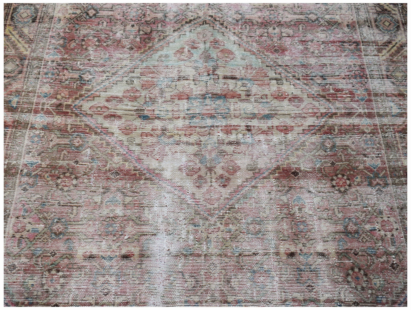 A vintage handwoven Persian rug featuring a faded diamond medallion pattern in muted tones.