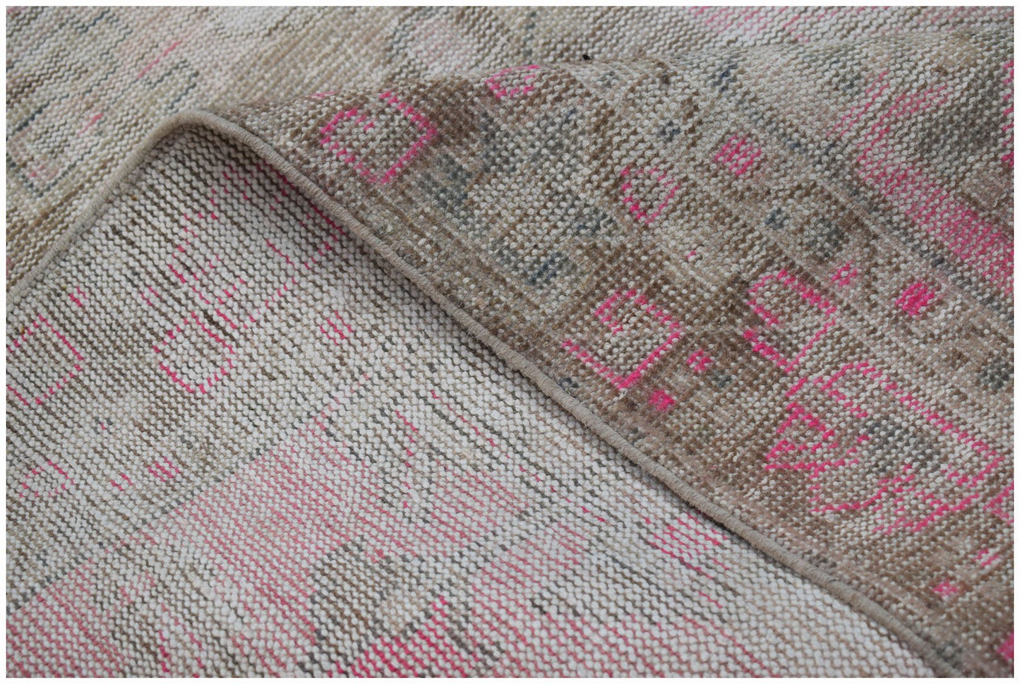 A vintage Persian rug featuring a distressed pattern in shades of beige and vibrant pink.