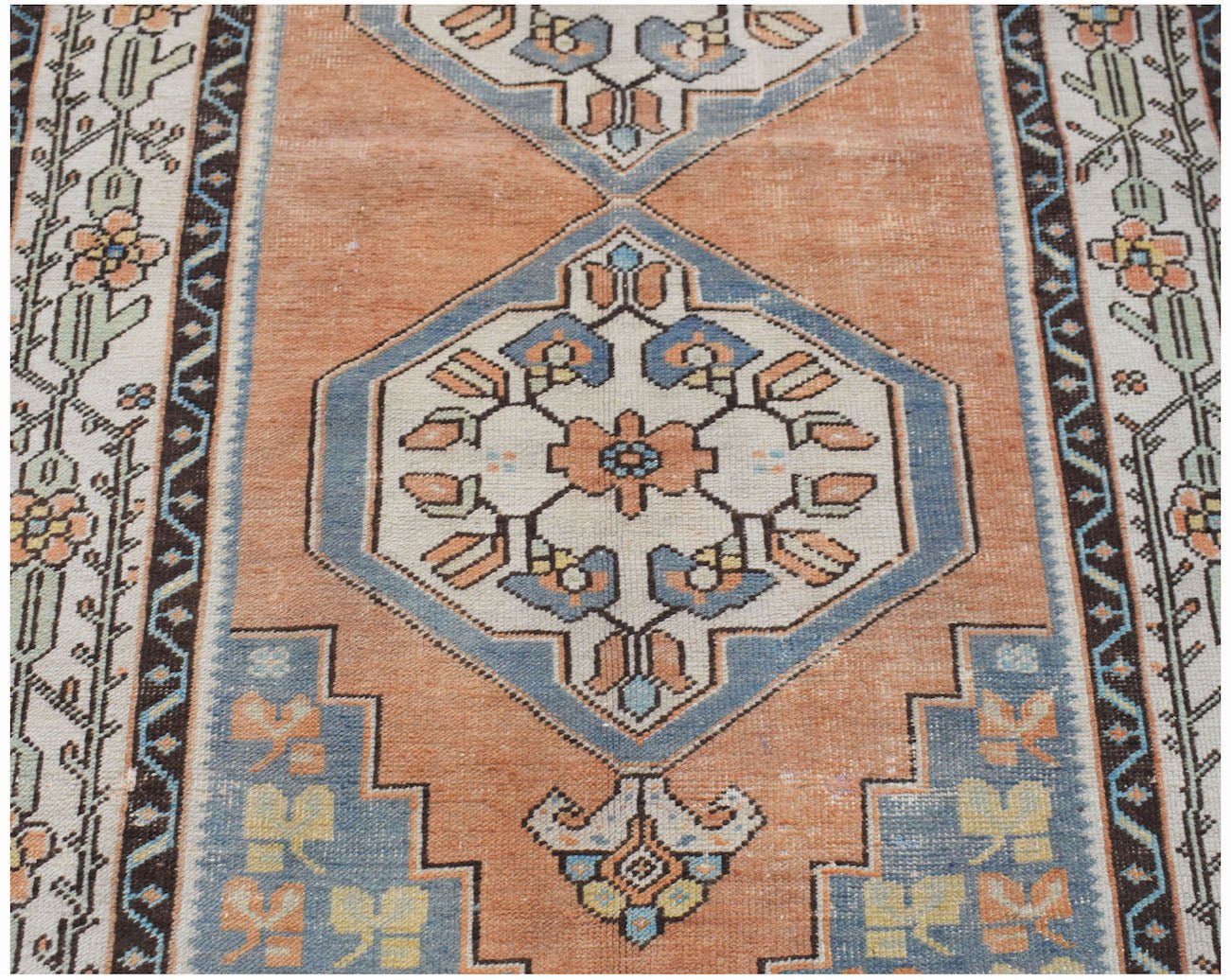 A vintage handwoven Persian rug featuring a geometric floral pattern in orange, blue, and cream.