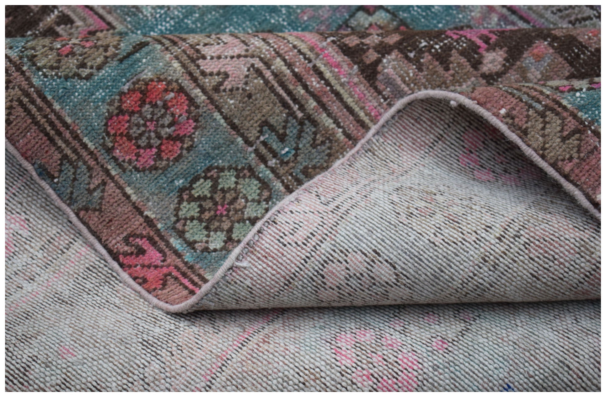 A vintage Persian Hamadan rug with a folded corner showing its wool pile and woven backing.