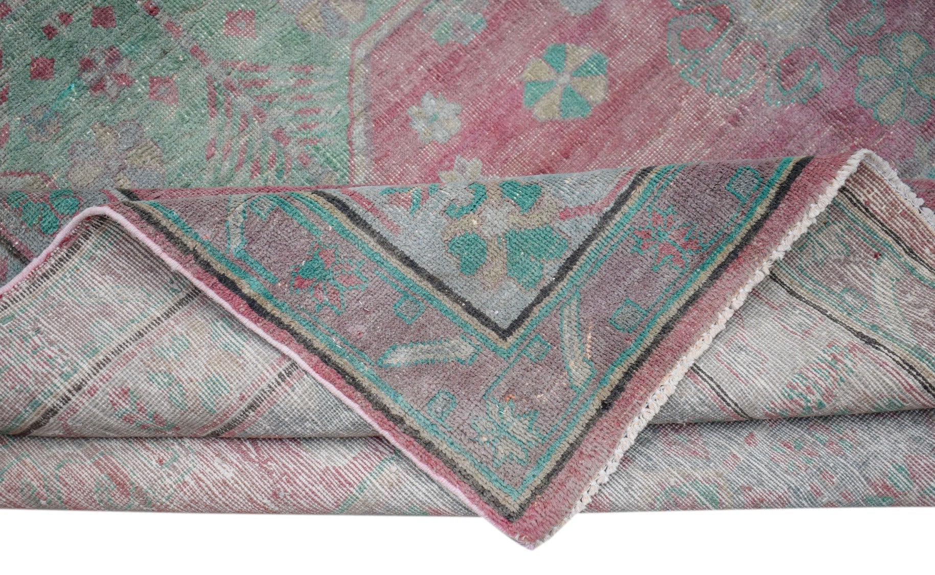 A vintage handwoven Persian rug featuring a faded floral pattern in shades of pink and green.