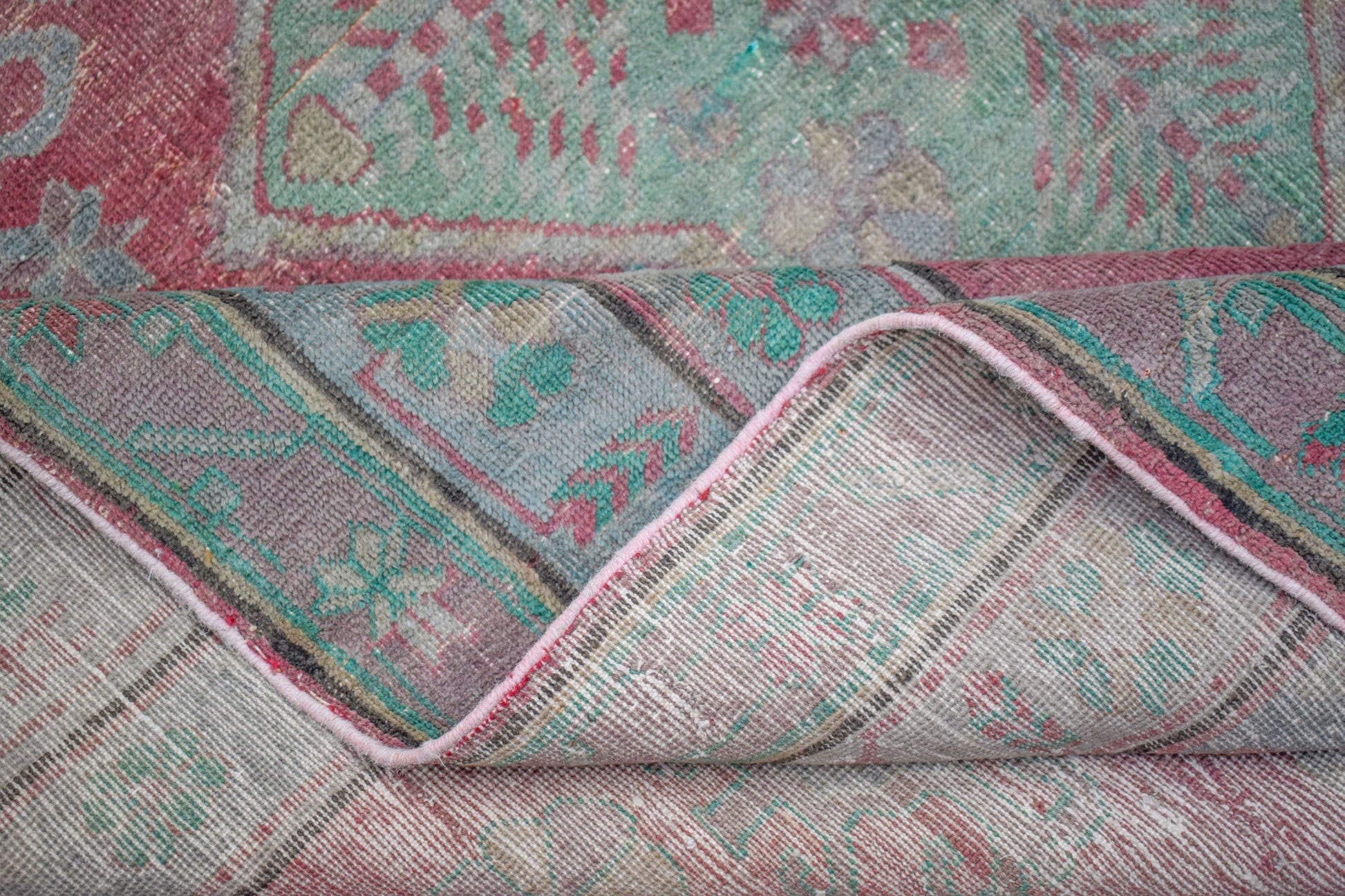A vintage handwoven Persian rug featuring a distressed floral pattern in shades of pink and green.
