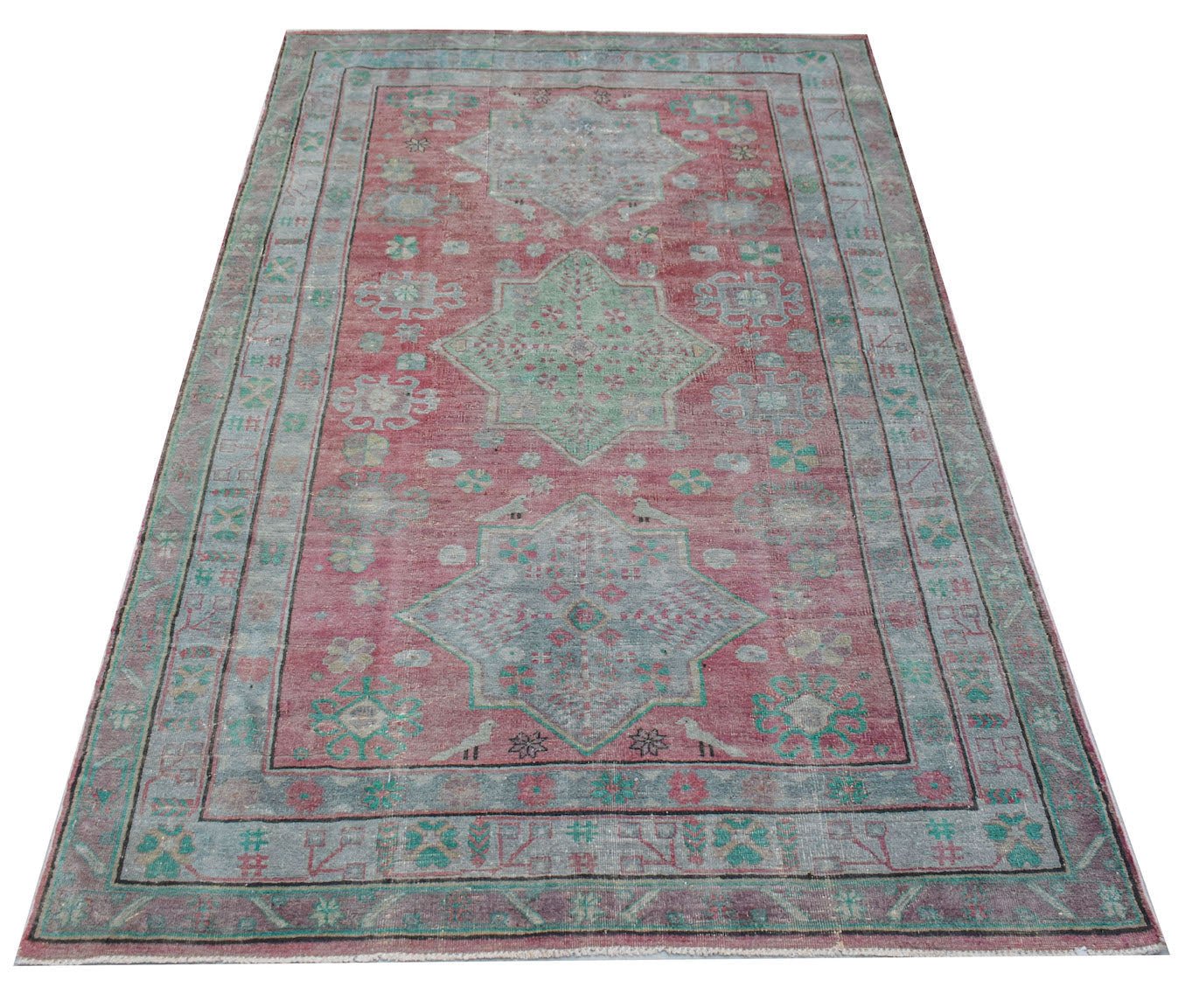 A vintage handwoven Persian rug featuring a faded red field with blue geometric medallions.