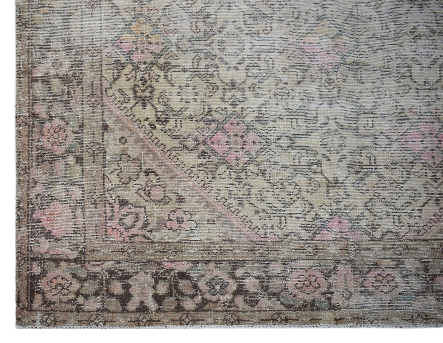A vintage handwoven Persian rug featuring a faded floral pattern in muted pink and brown tones.