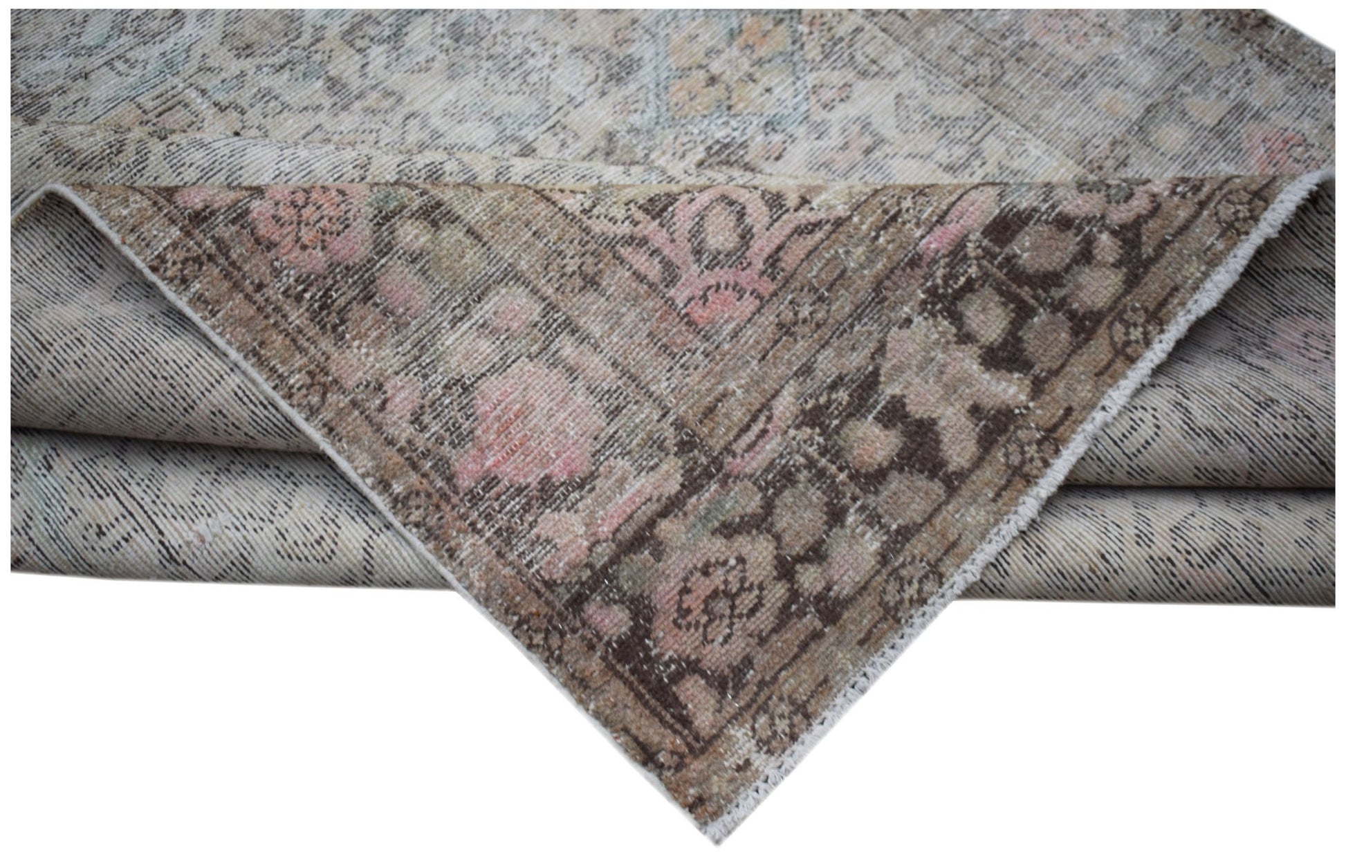 A vintage handwoven Persian rug featuring a faded floral pattern in muted pink and brown tones.
