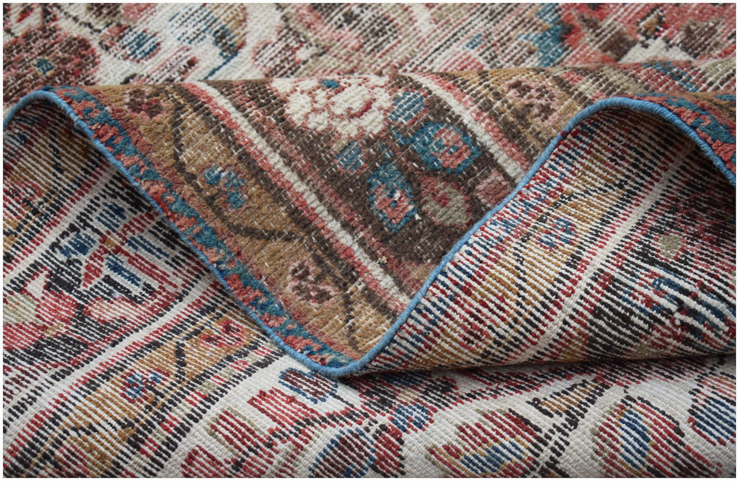 A handwoven vintage Persian rug featuring a worn, intricate floral pattern in red, blue, and brown.
