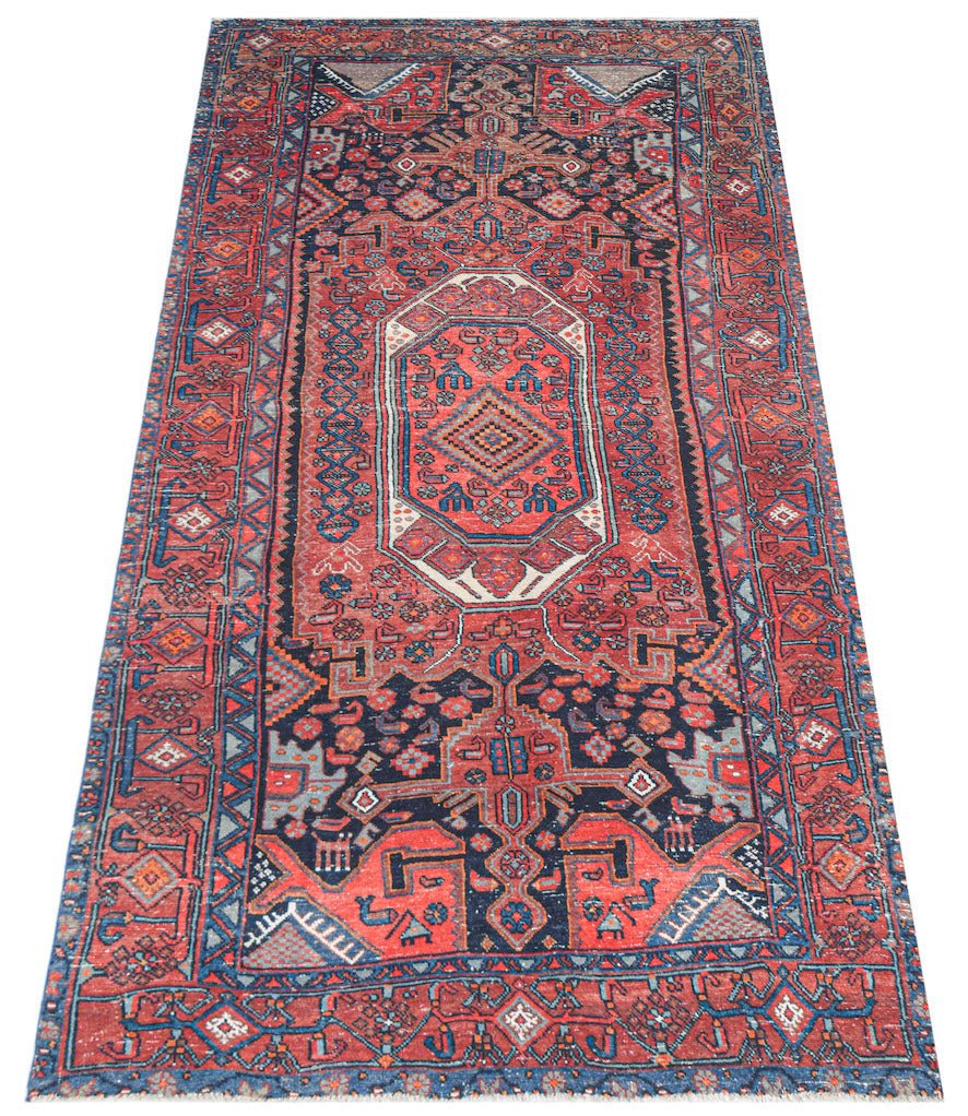 A handwoven vintage Persian rug featuring a geometric medallion pattern in red, blue, and cream.