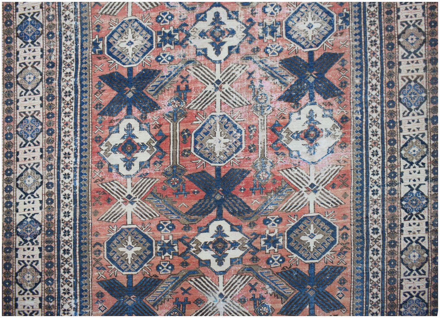 A vintage handwoven Persian rug featuring geometric patterns in shades of red, blue, and cream.