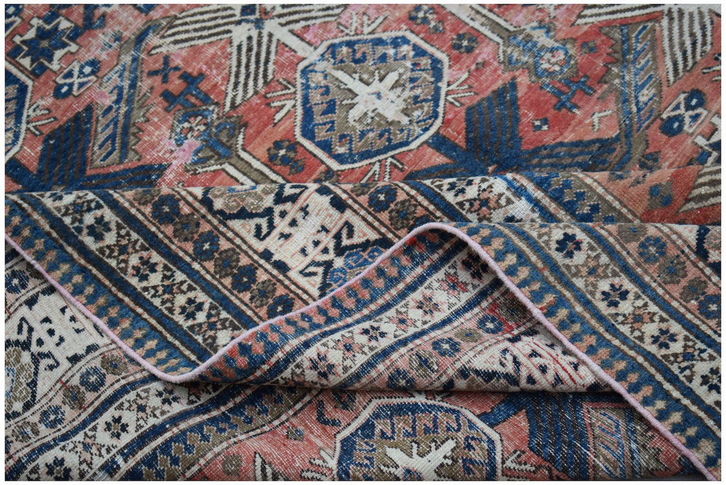 A handwoven vintage Persian rug featuring a geometric pattern in shades of red, blue, and cream.