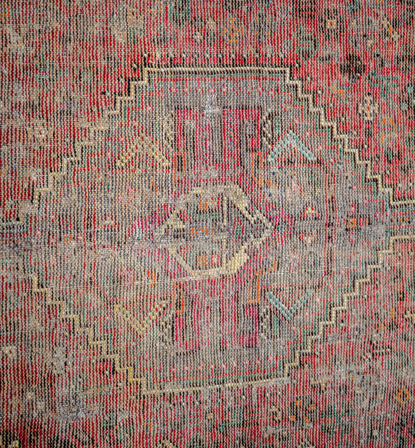 A vintage Persian rug featuring a faded geometric medallion pattern in red and grey tones.
