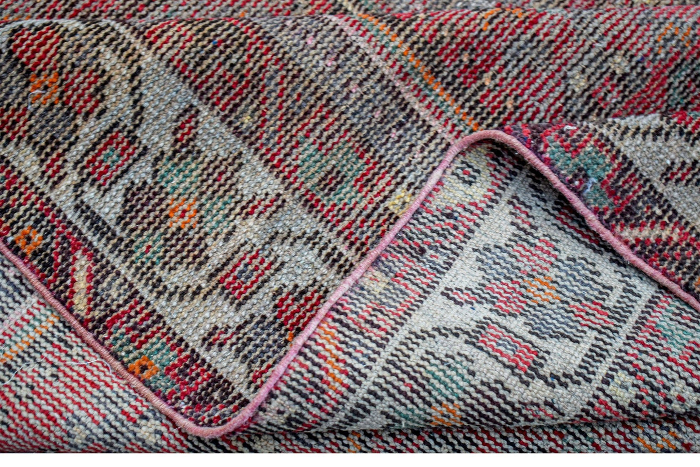 A folded vintage Persian rug featuring intricate patterns in red, grey, and orange wool.