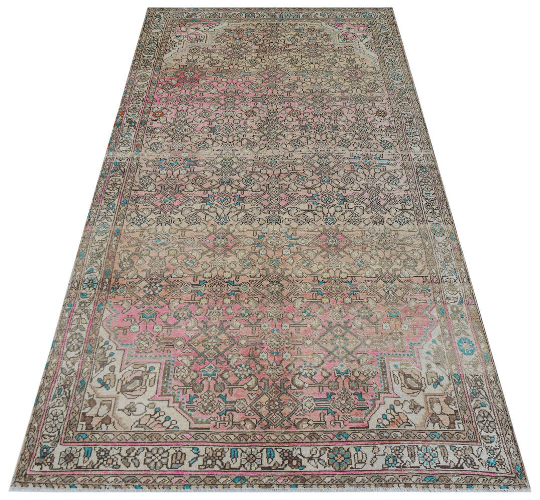 A handwoven vintage Persian rug featuring a faded floral pattern in pink, blue, and beige tones.