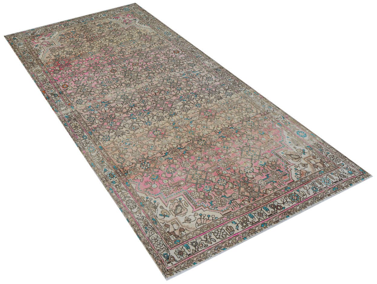 A handwoven vintage Persian rug featuring a faded floral pattern in shades of pink and beige.