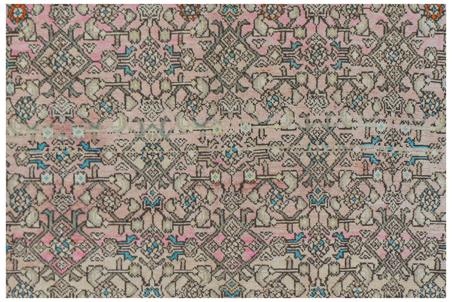 A vintage handwoven Persian rug featuring an intricate geometric pattern in pink and neutral tones.