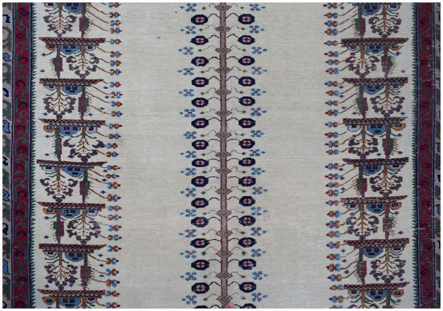 A vintage handwoven Persian rug featuring a cream field with repeating floral and tree motifs.