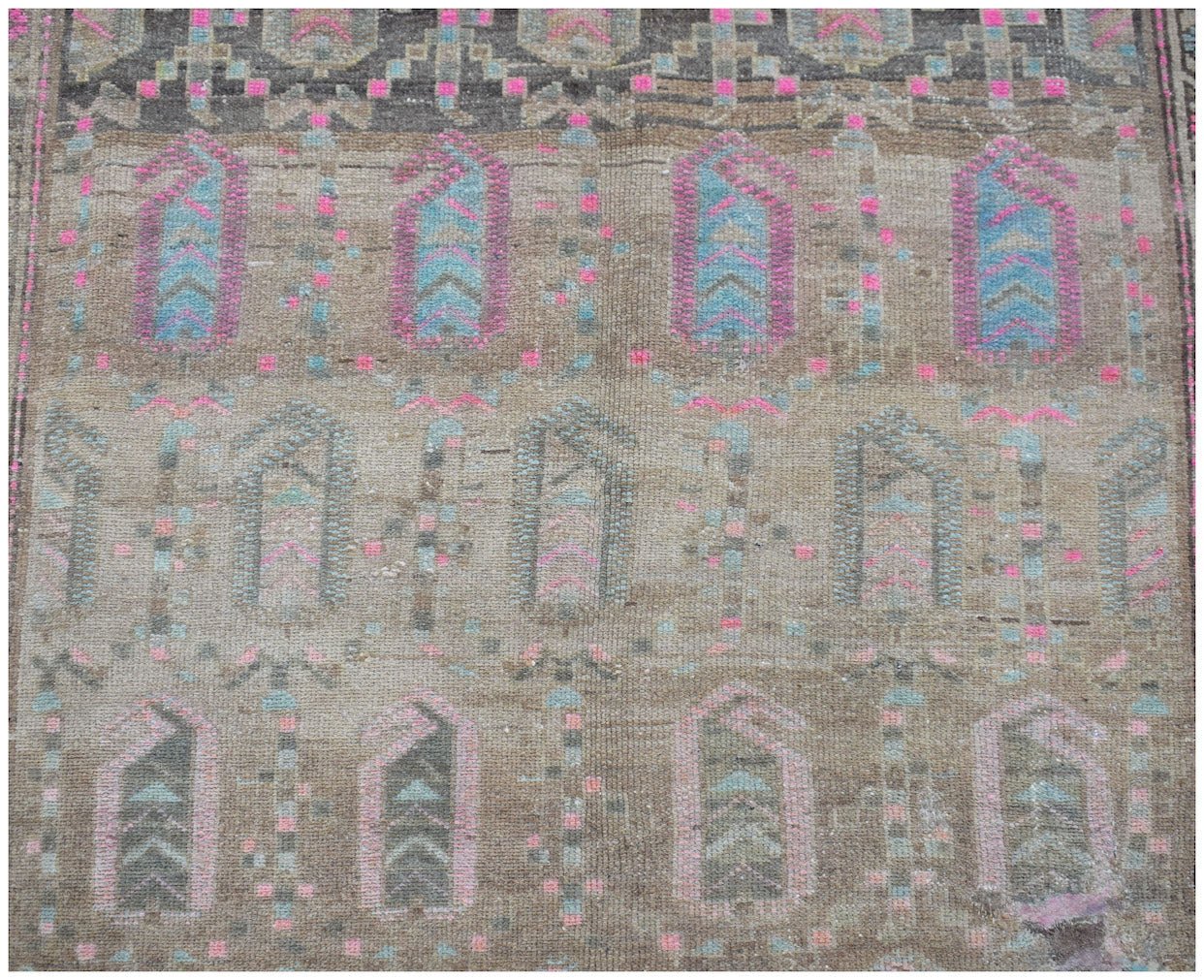 A vintage handwoven Persian rug featuring a repeating geometric pattern in muted brown and pink.