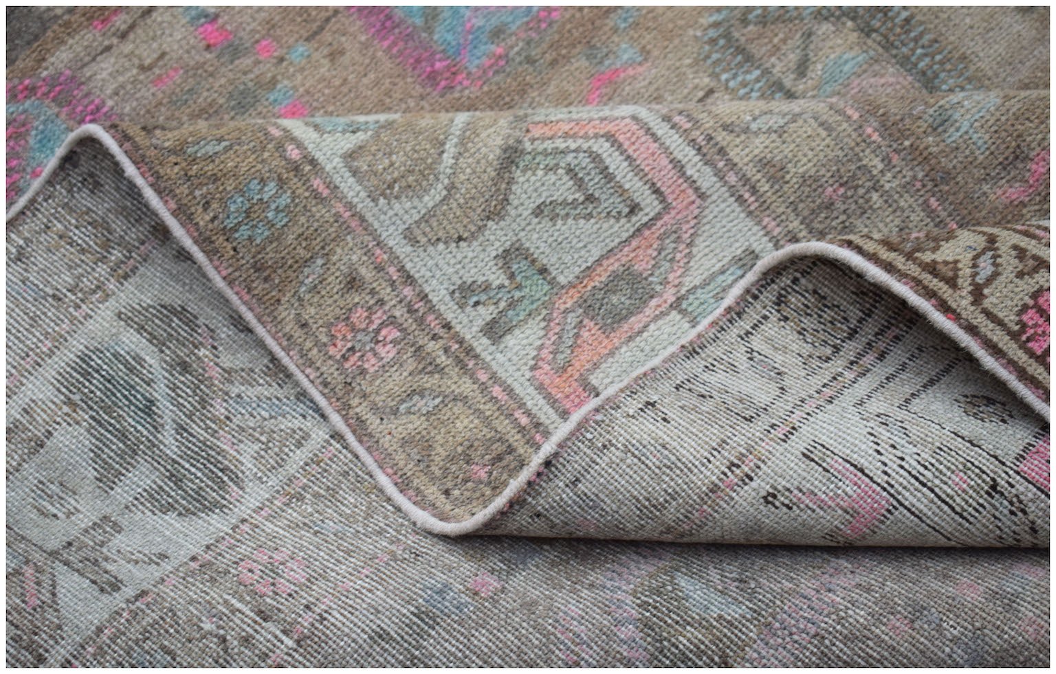 A vintage handwoven Persian rug featuring a faded geometric pattern in muted pink and blue tones.