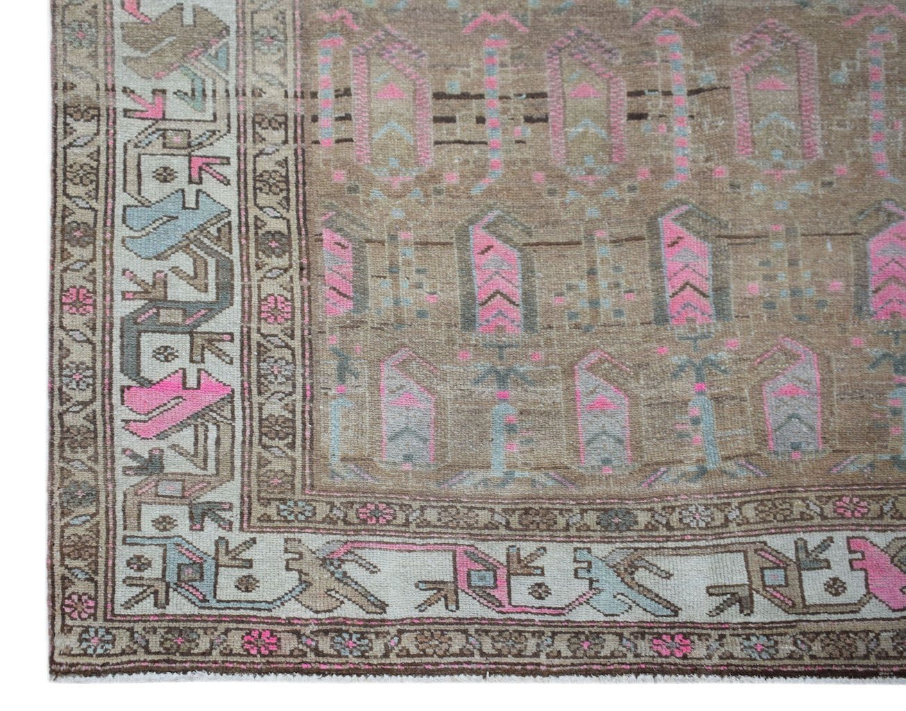 A vintage handwoven Persian rug featuring geometric patterns in brown, pink, and blue tones.
