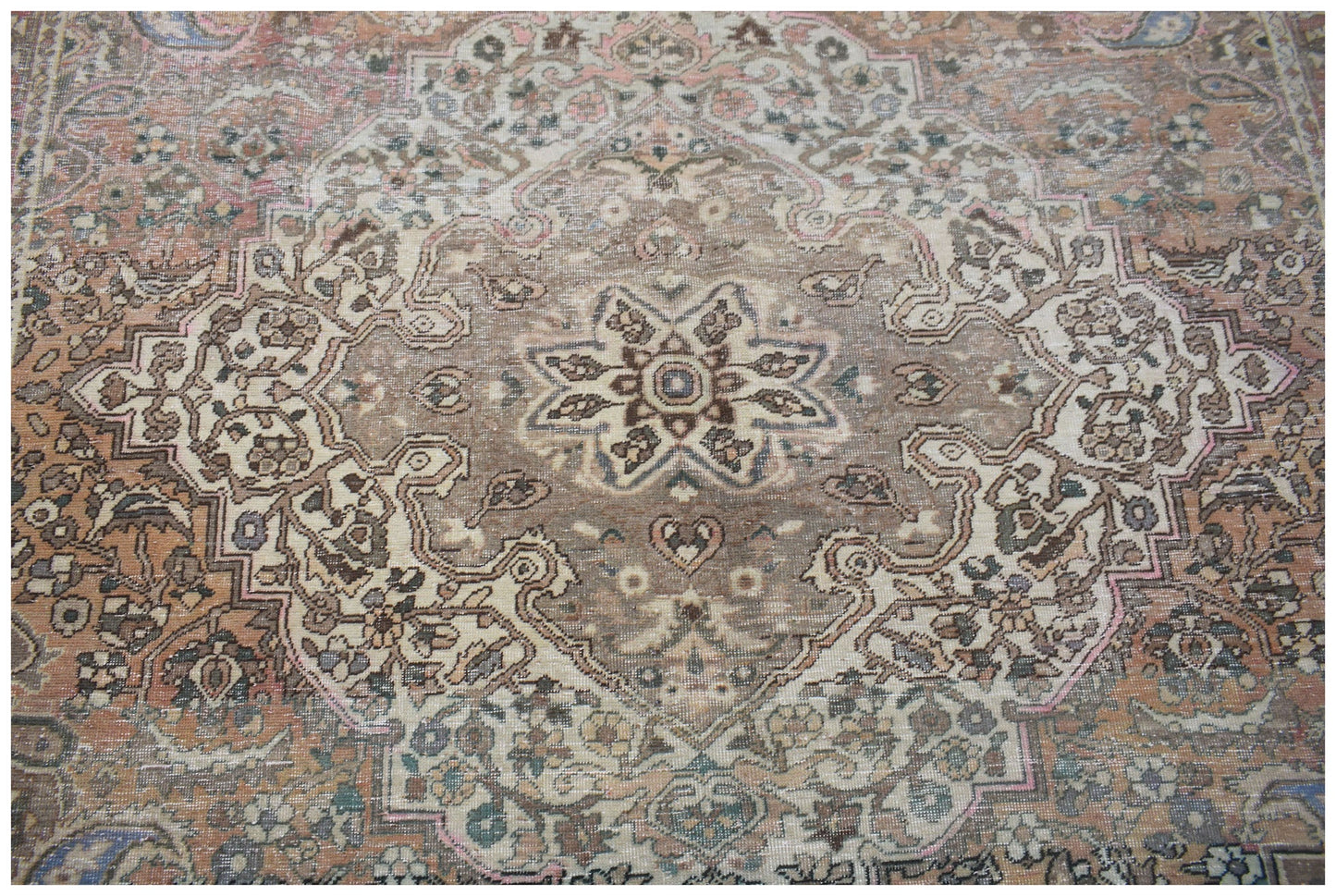 A vintage handwoven Persian rug featuring a central floral medallion in muted earth tones.