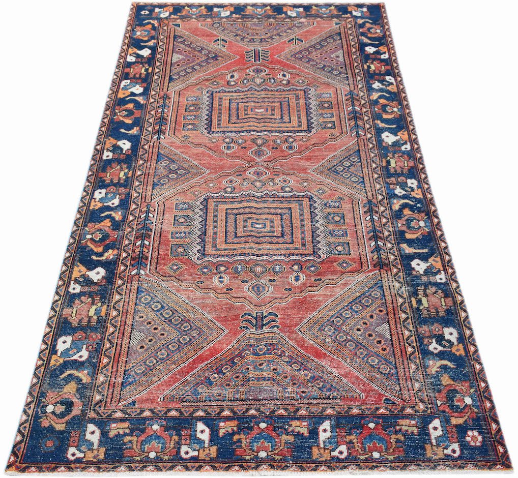 A handwoven vintage Persian rug featuring geometric patterns in red and blue tones.