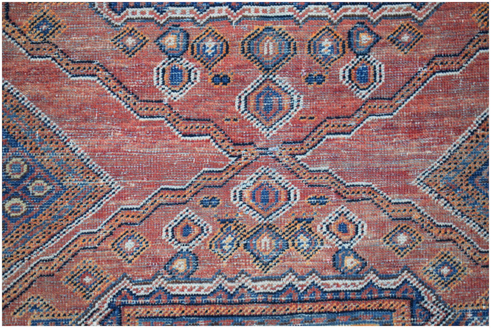 A vintage handwoven Persian rug featuring a geometric pattern in shades of red, blue, and orange.