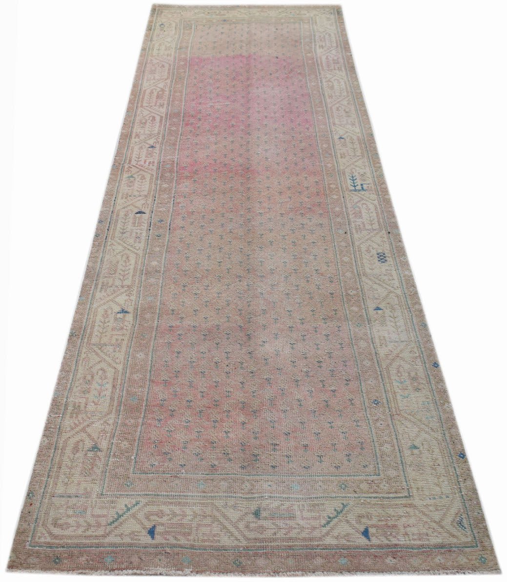 A long, handwoven vintage Persian runner rug featuring a faded pink center and patterned borders.