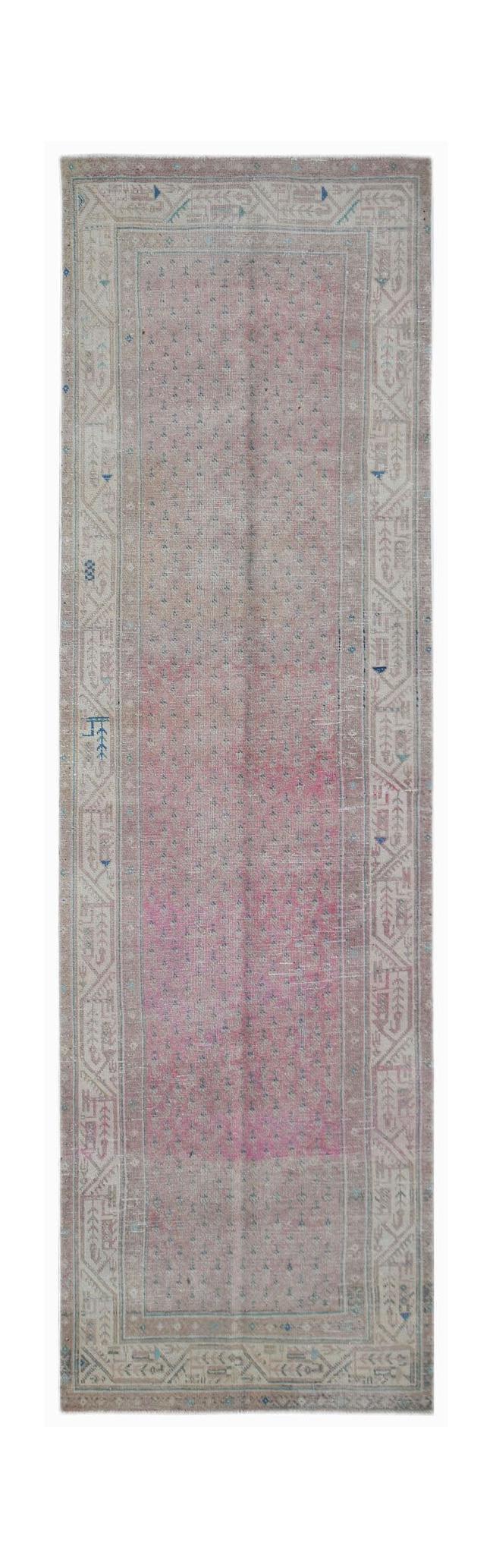 A long, handwoven vintage Persian runner rug featuring a faded pink center and geometric borders.