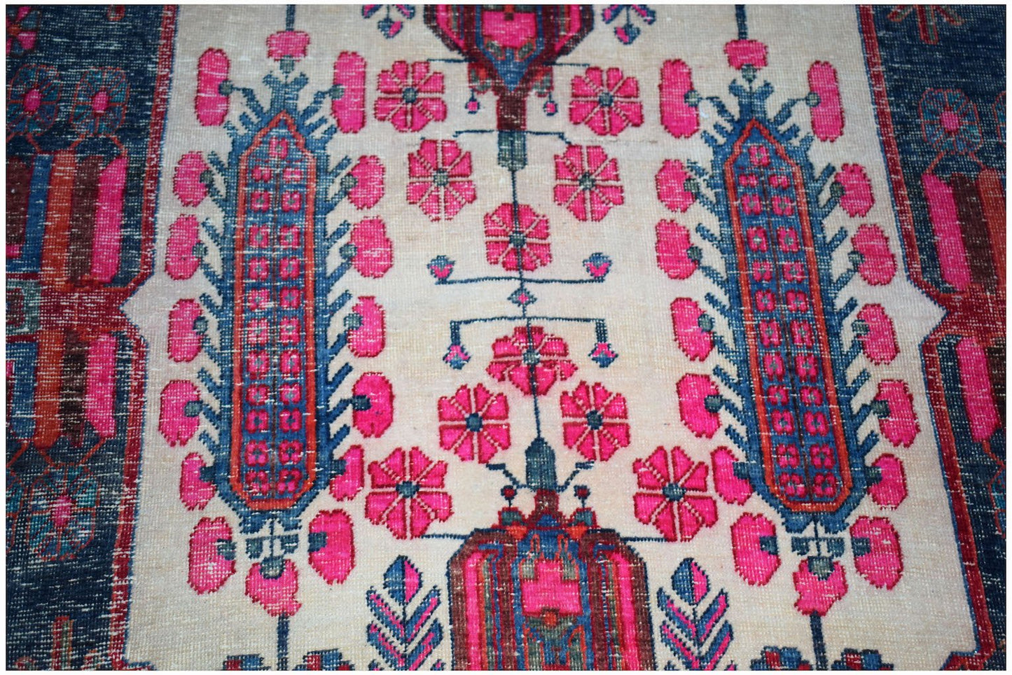 A vintage handwoven Persian rug featuring a floral pattern in vibrant pink and blue on a cream base.