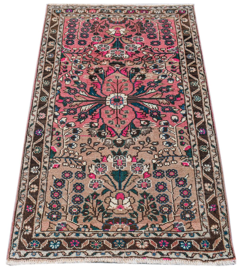 A vintage Persian Sarouk rug featuring a floral medallion pattern in pink, brown, and teal tones.